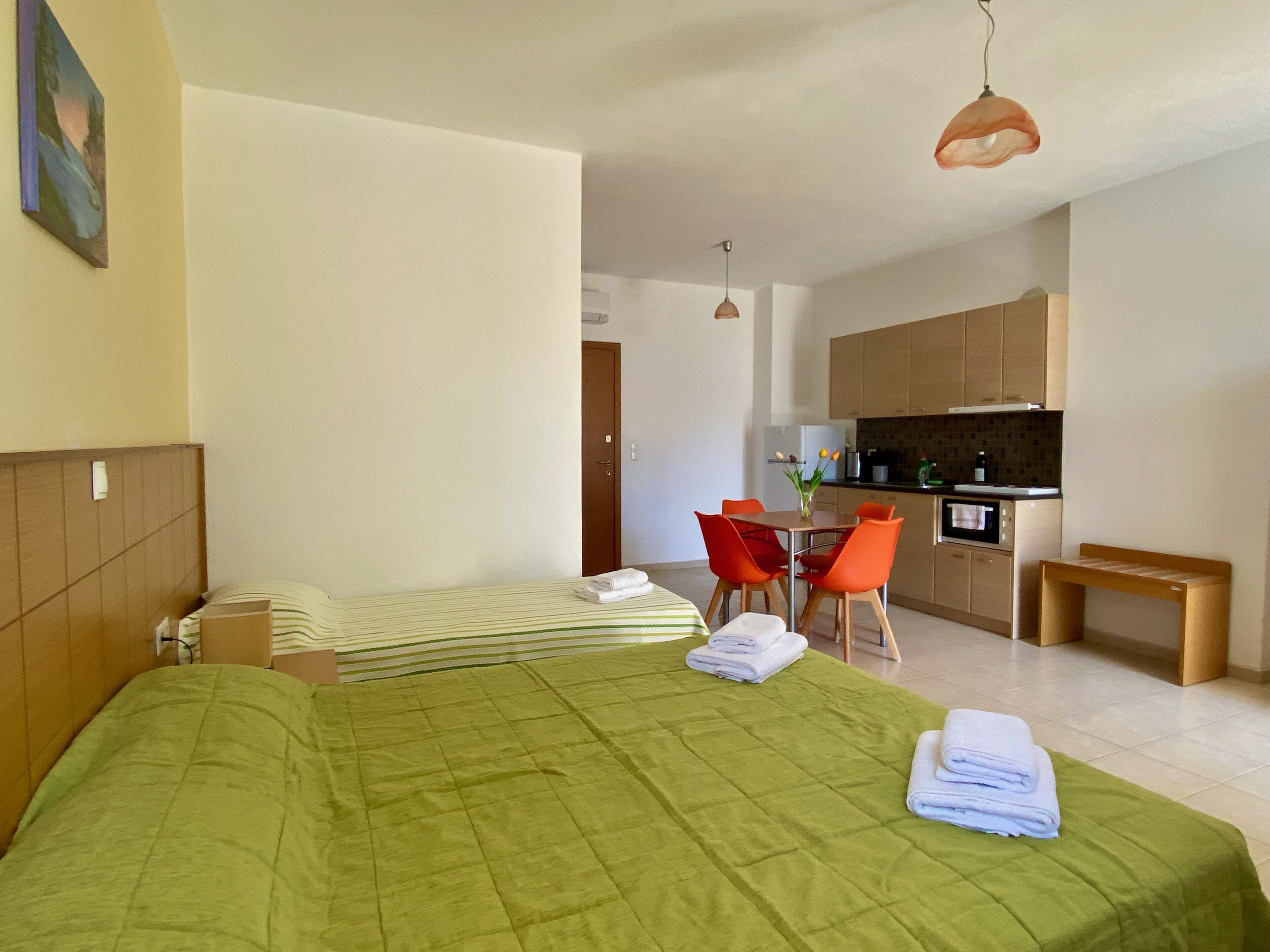 A hotel room with a bed, a small table with chairs, a kitchenette, and a bathroom.