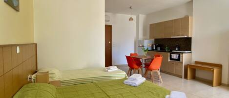 A hotel room with a bed, a small table with chairs, a kitchenette, and a bathroom.