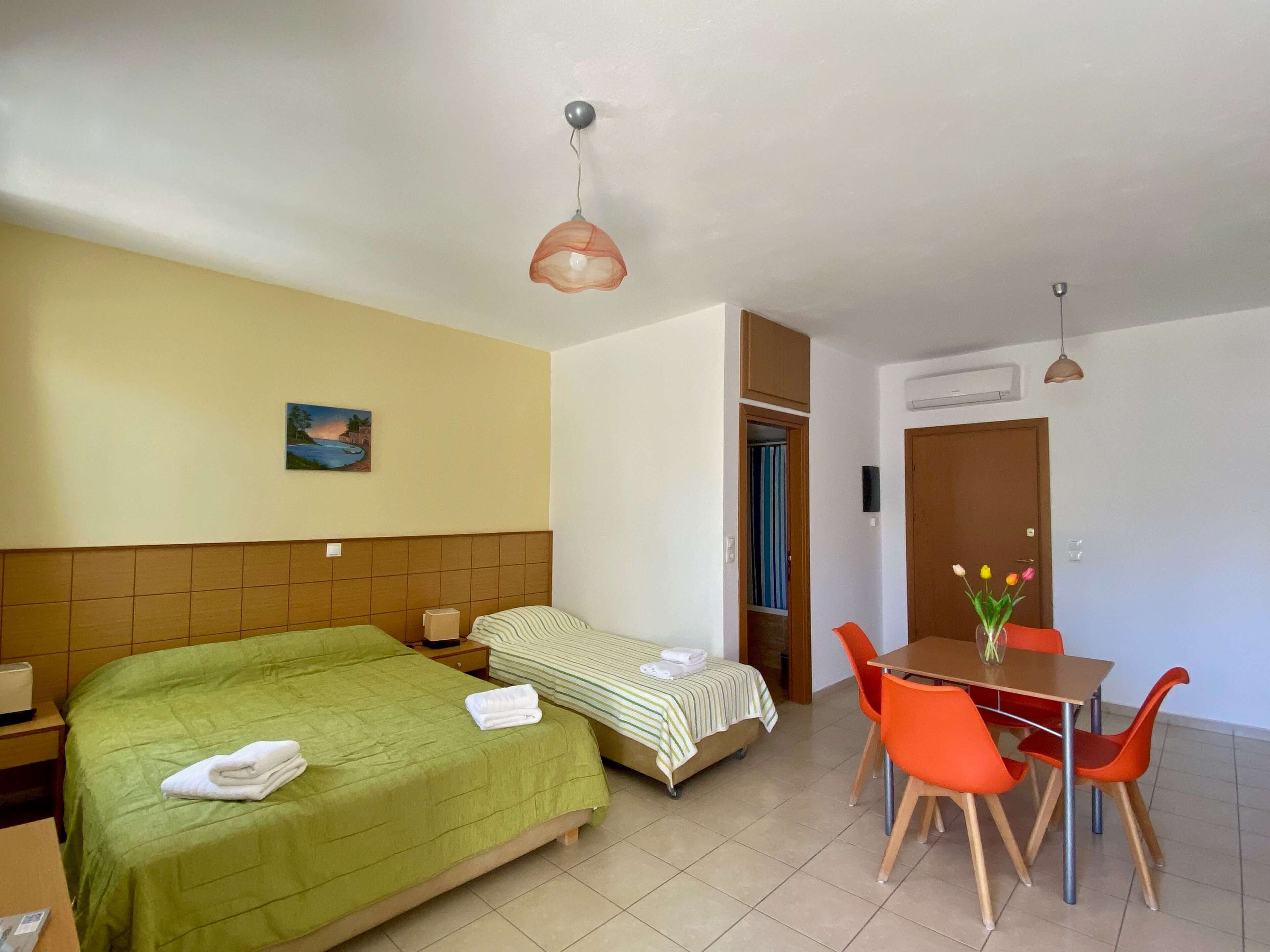 A hotel room with a bed, a small table with chairs, a painting on the wall, and a door leading to a closet.