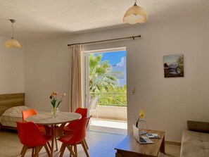 A room with a dining table, red chairs, a laptop, and a painting on the wall.