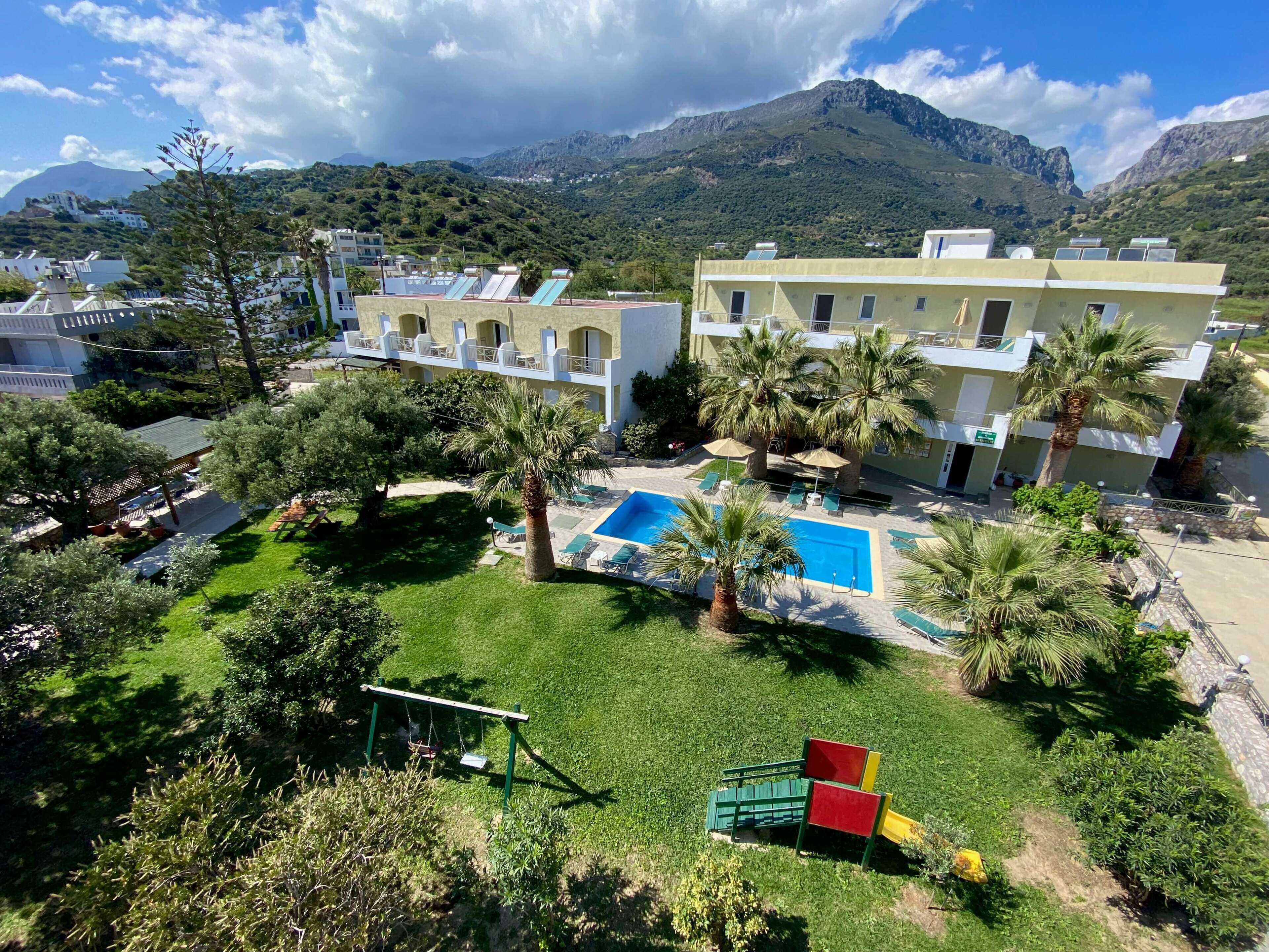 A hotel with a swimming pool, palm trees, and a mountainous backdrop.
