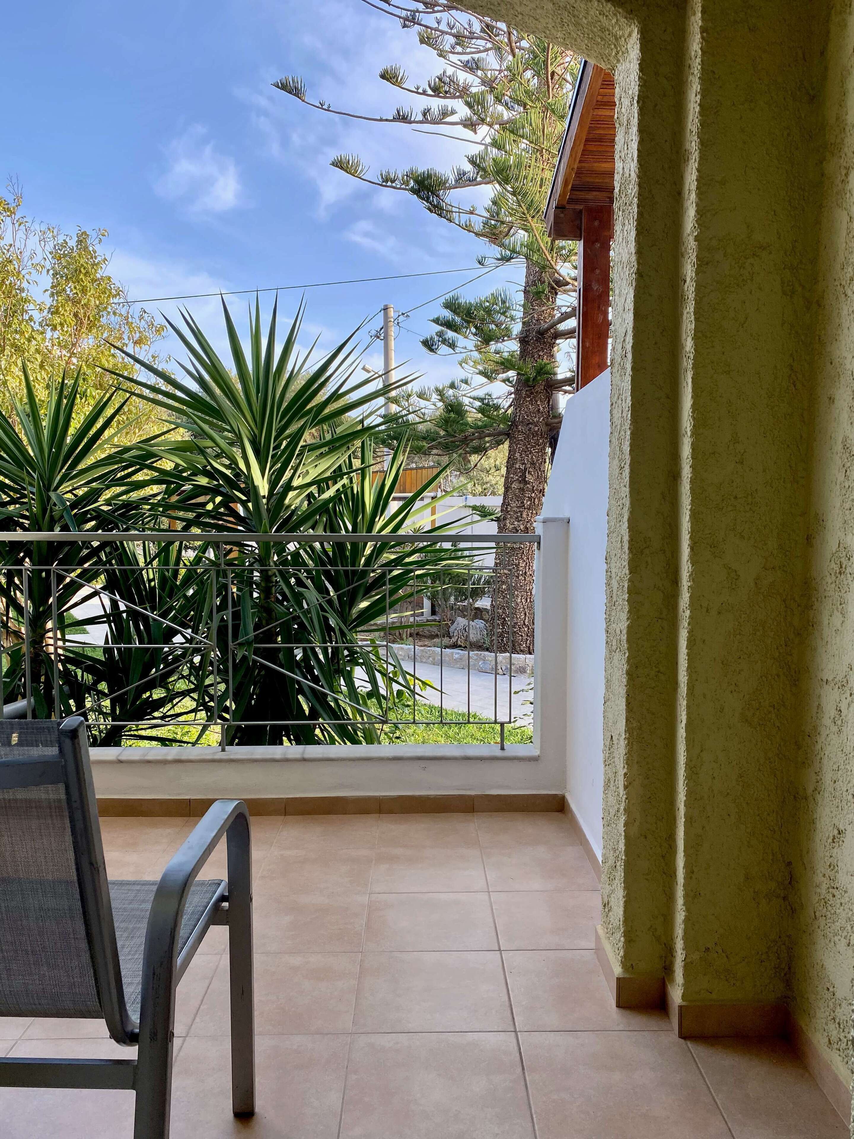 Un balcon avec une chaise, un pot de fleurs et une vue sur une rue et des arbres.