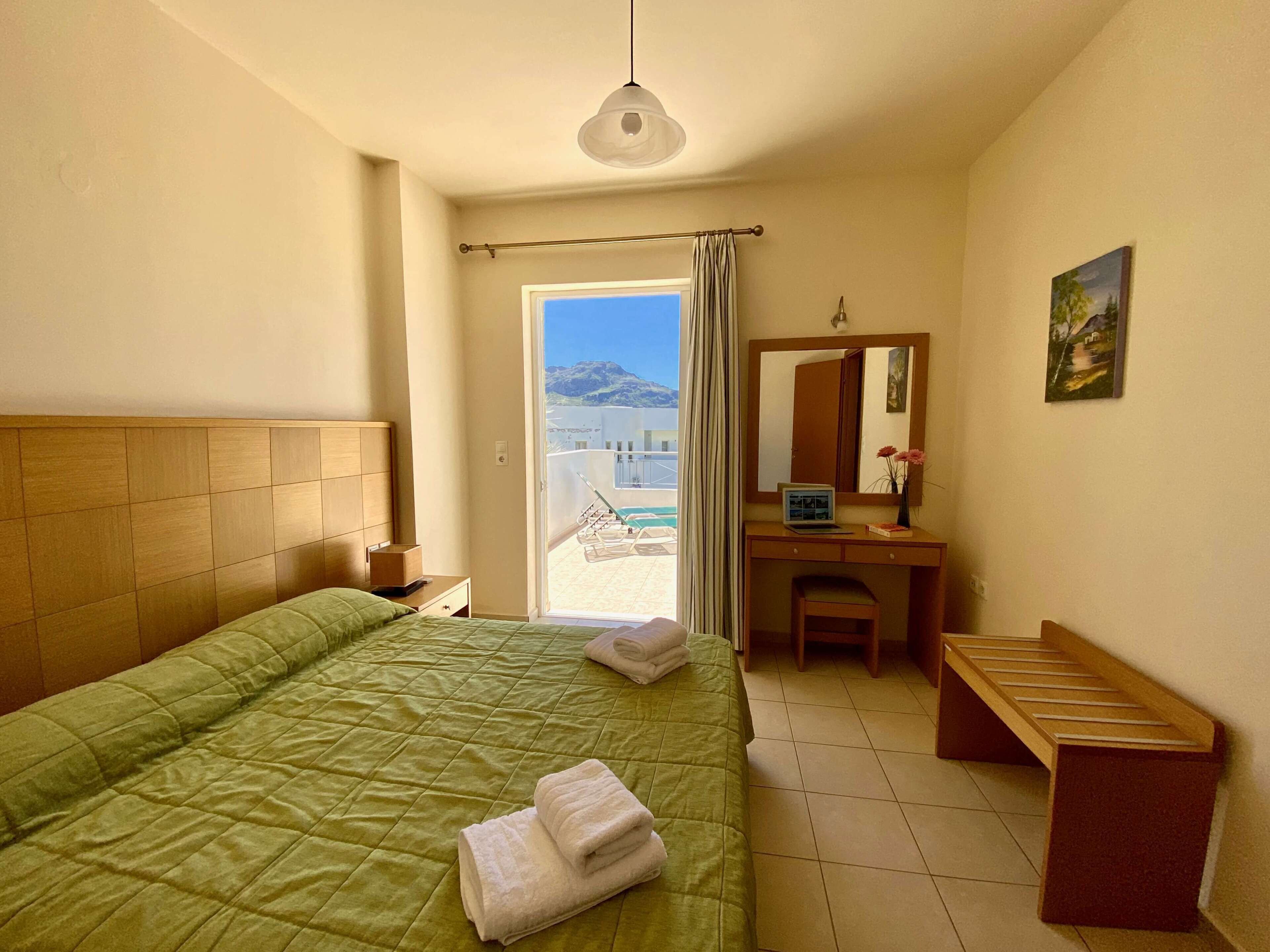 A hotel room with a bed, a desk, a chair, a mirror, and a view of the beach.