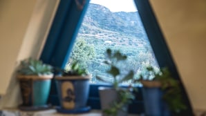 Une vue par la fenêtre sur un paysage montagneux, avec des plantes en pot sur le rebord de la fenêtre.