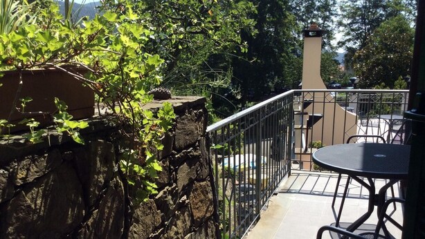Un balcón con pared de piedra, barandilla de metal y una mesa con sillas.