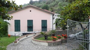 Un edificio rosa con contraventanas verdes, un camino de piedra y una reja de metal.