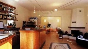 Zona de bar con mostrador y estanterías llenas de botellas, área de estar con alfombra y chimenea al fondo.