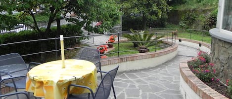 An outdoor patio area with stone flooring, metal chairs, and tables covered with yellow tablecloths.