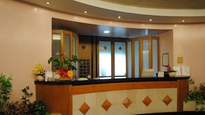 A reception desk with a curved design, a glass partition, and a tiled lower section. There are potted plants and a framed certificate on the wall. - Meranda (Spezzano della Sila)