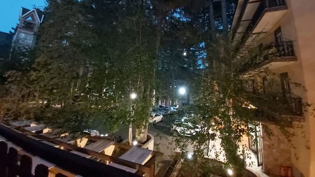A nighttime view of a narrow street with buildings on either side, trees lining the street, and a few parked cars. - Meranda (Spezzano della Sila)