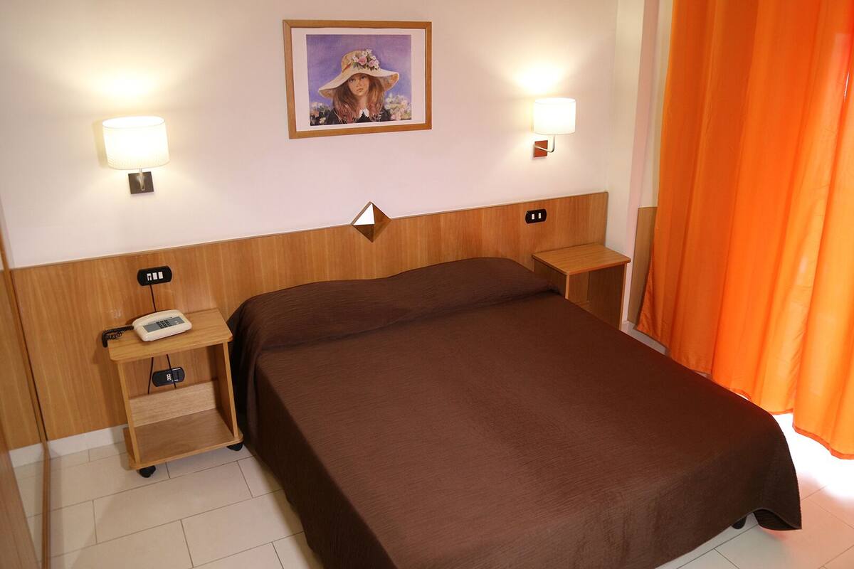 A hotel room with a large bed, two bedside tables, a telephone, and a painting on the wall.