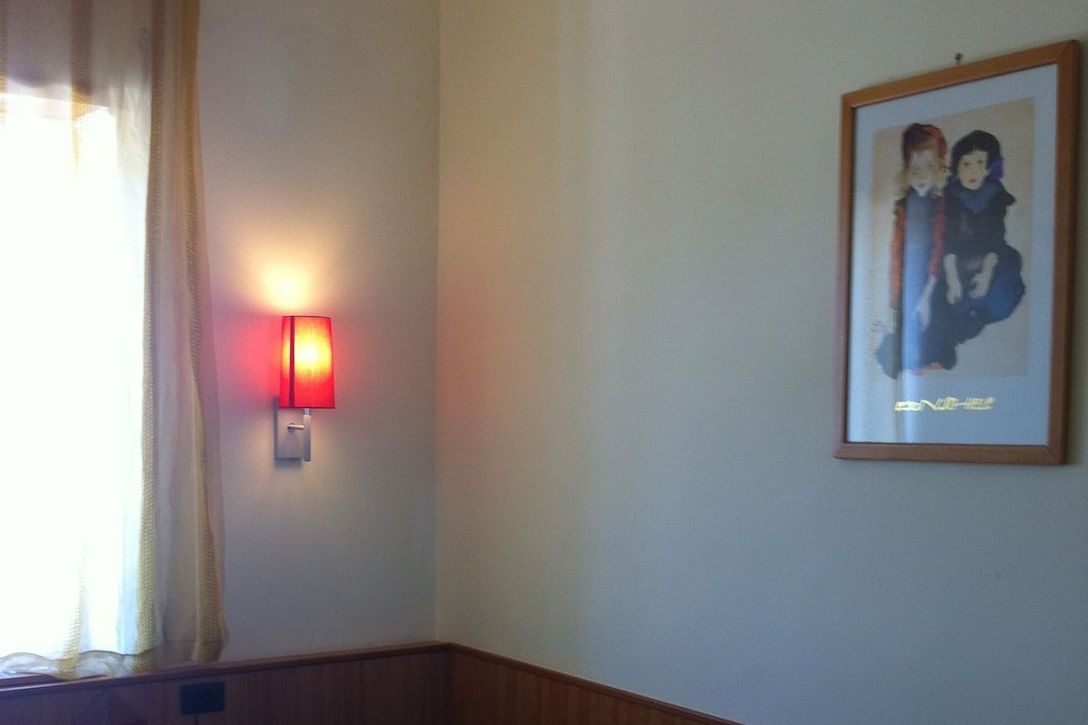 A small, single-bed room with a wooden headboard, a bedside table with a phone, a wall-mounted light, and a framed picture on the wall.