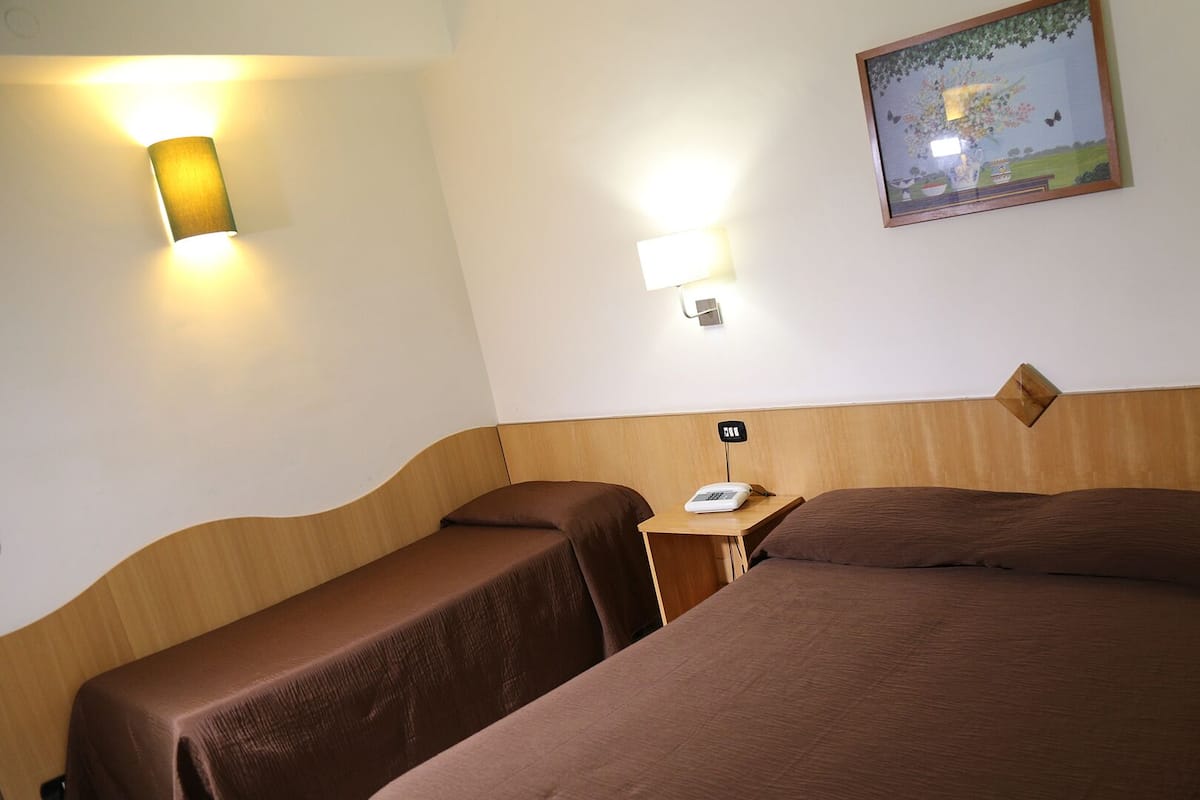 A hotel room with two single beds, a wooden headboard, a nightstand with a telephone, and two wall-mounted lamps.