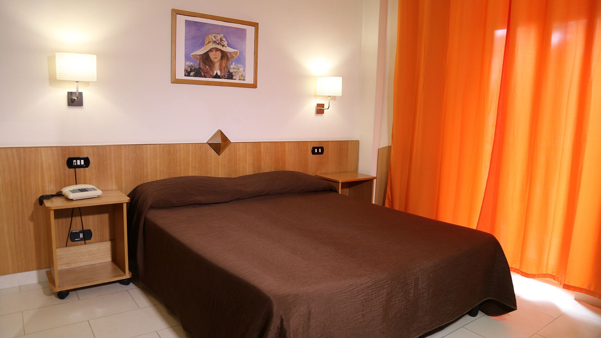 Una habitación de hotel con una cama, dos mesitas de noche, un teléfono y un cuadro en la pared.
