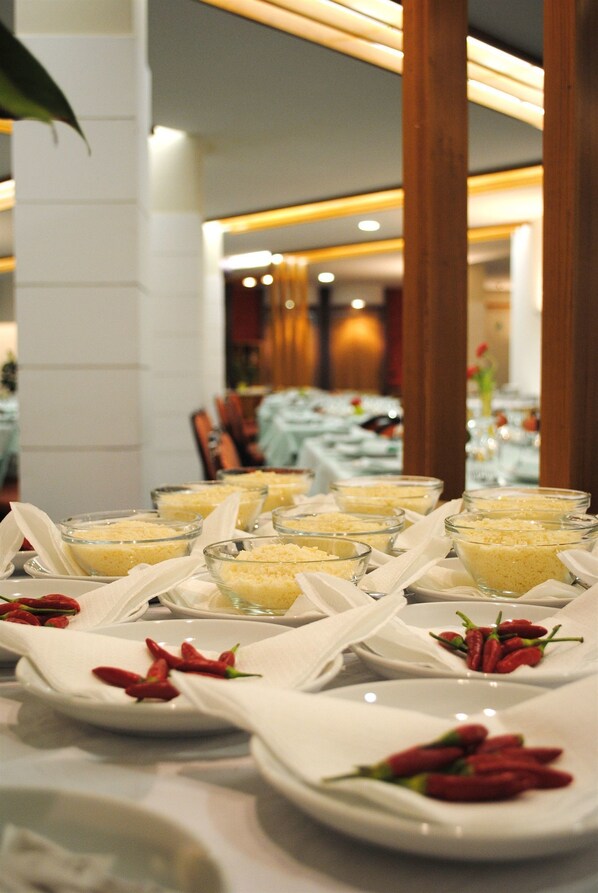 Una mesa de buffet con recipientes de vidrio transparentes llenos de comida, servilletas blancas y chiles rojos en platos.