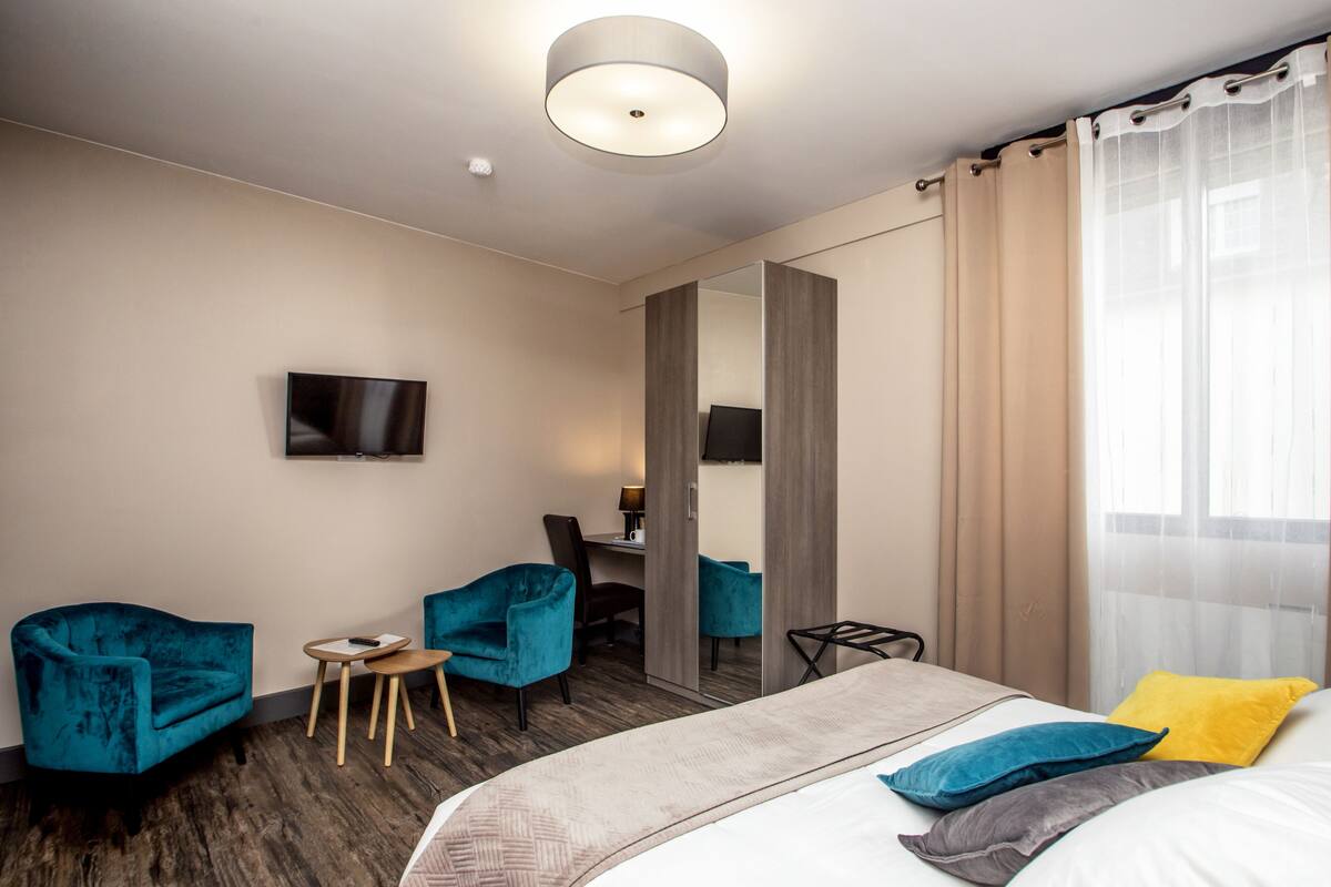 A hotel room with a bed, two chairs, a small table, a TV, and a mirror.