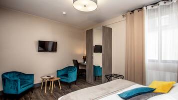 A hotel room with a bed, two chairs, a small table, a TV, and a mirror.