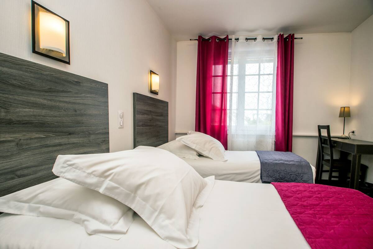 A hotel room with two beds, a desk, and a chair.