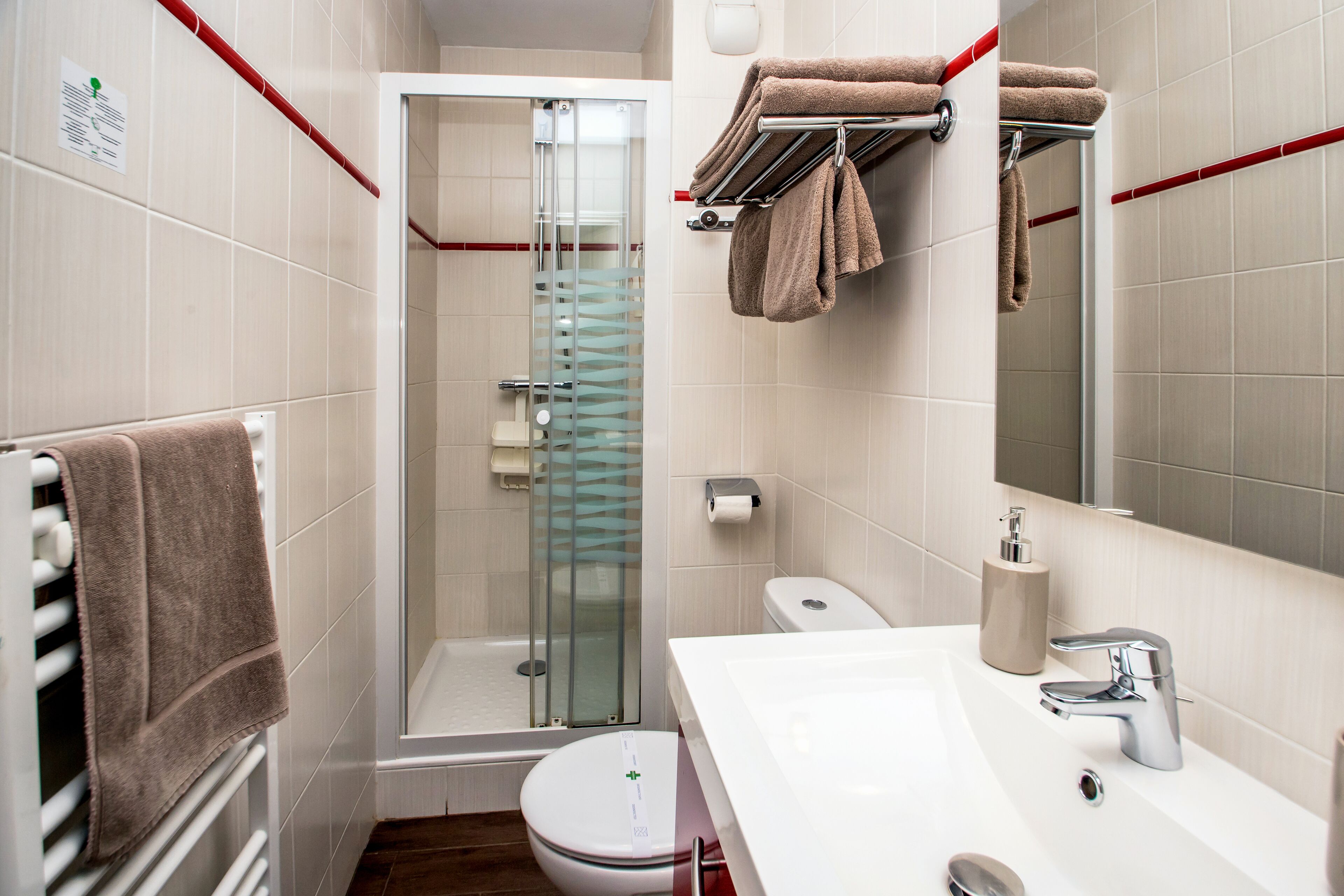 A bathroom with a glass shower enclosure, a toilet, a sink with a mirror, and towels on a rack.
