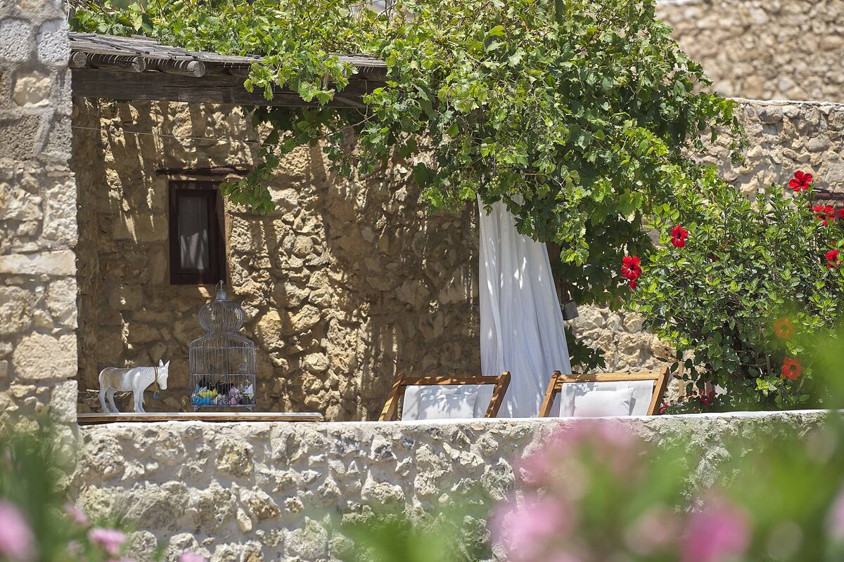 A stone building with a small window, a white curtain, and a birdcage with colorful items.