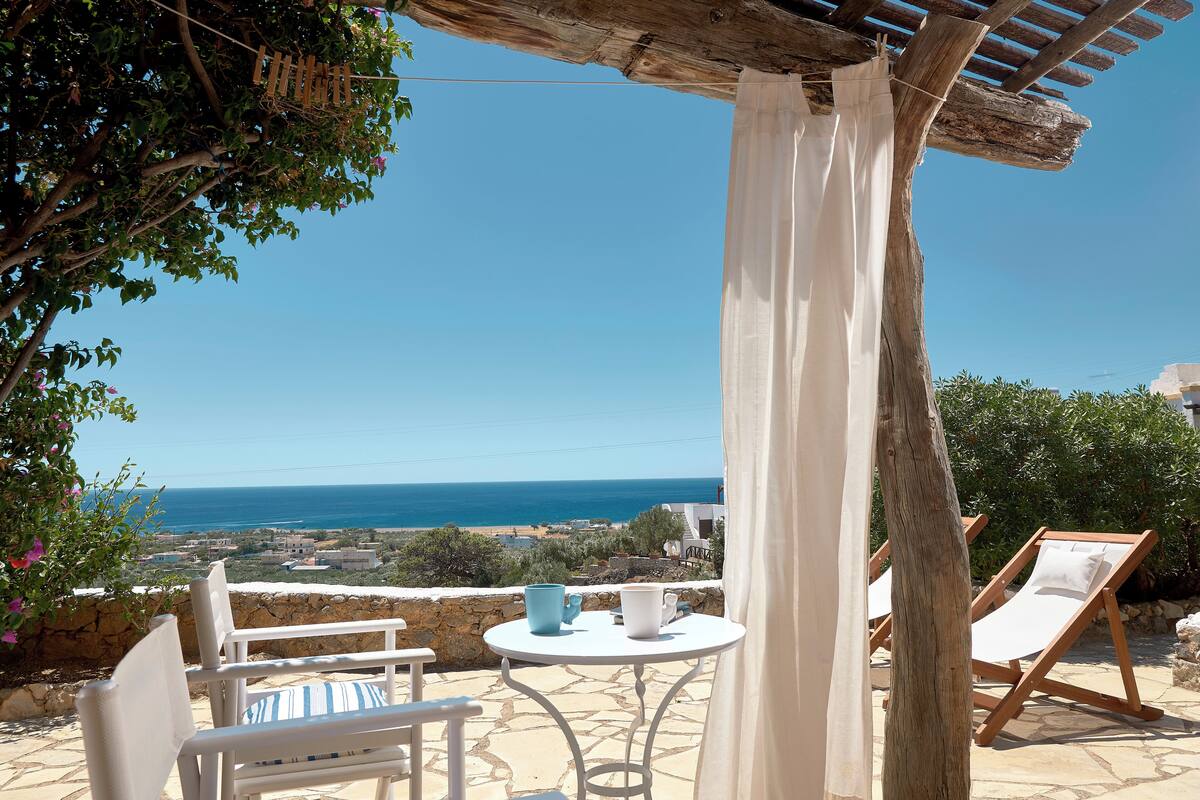 A terrace with a table and chairs, overlooking a coastal view.