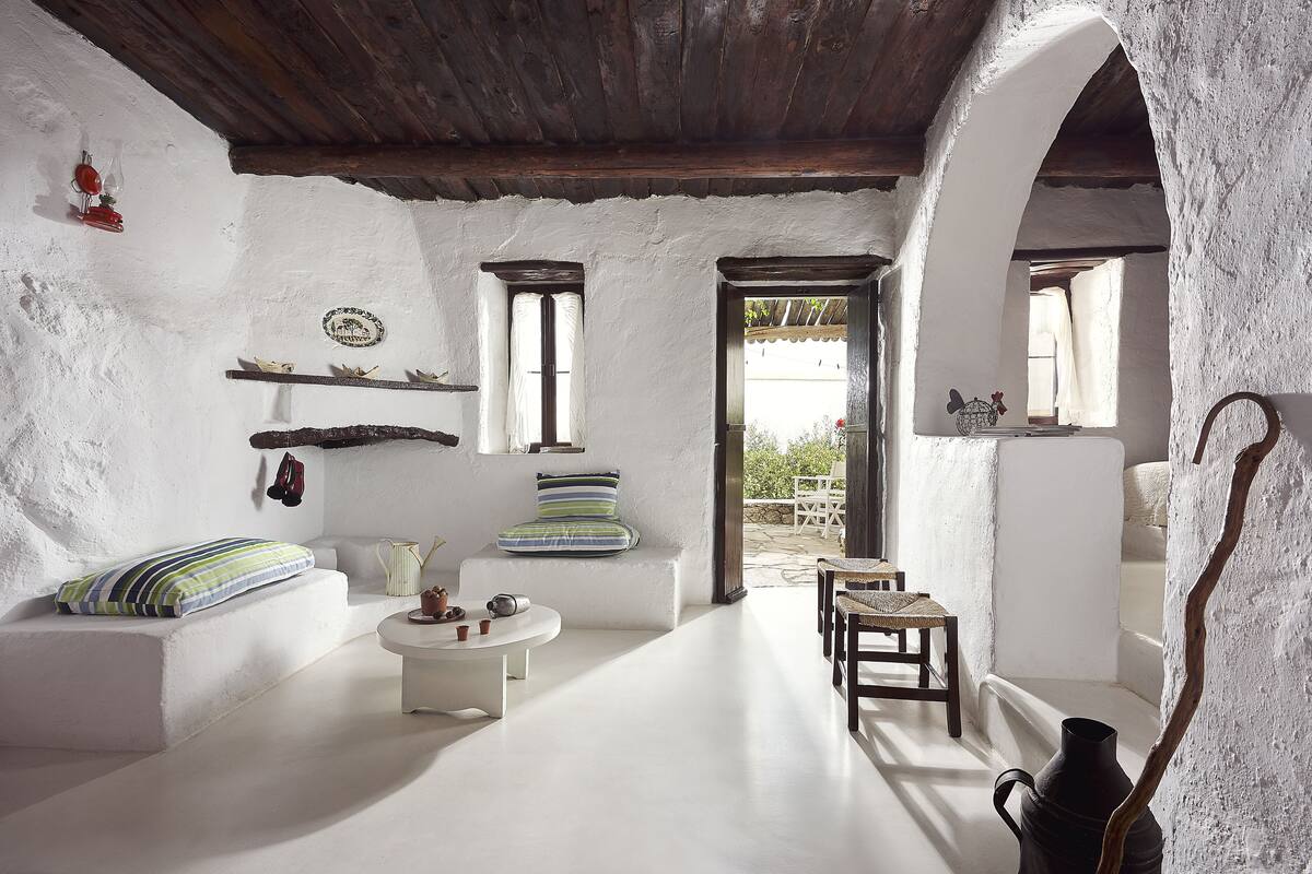 A rustic interior with white walls, wooden beams, a stone fireplace, and a view to the outside.