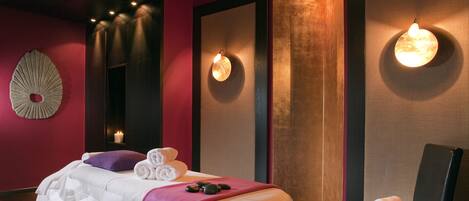 A room with a bed, a massage table, a chair, and wall-mounted lights.
