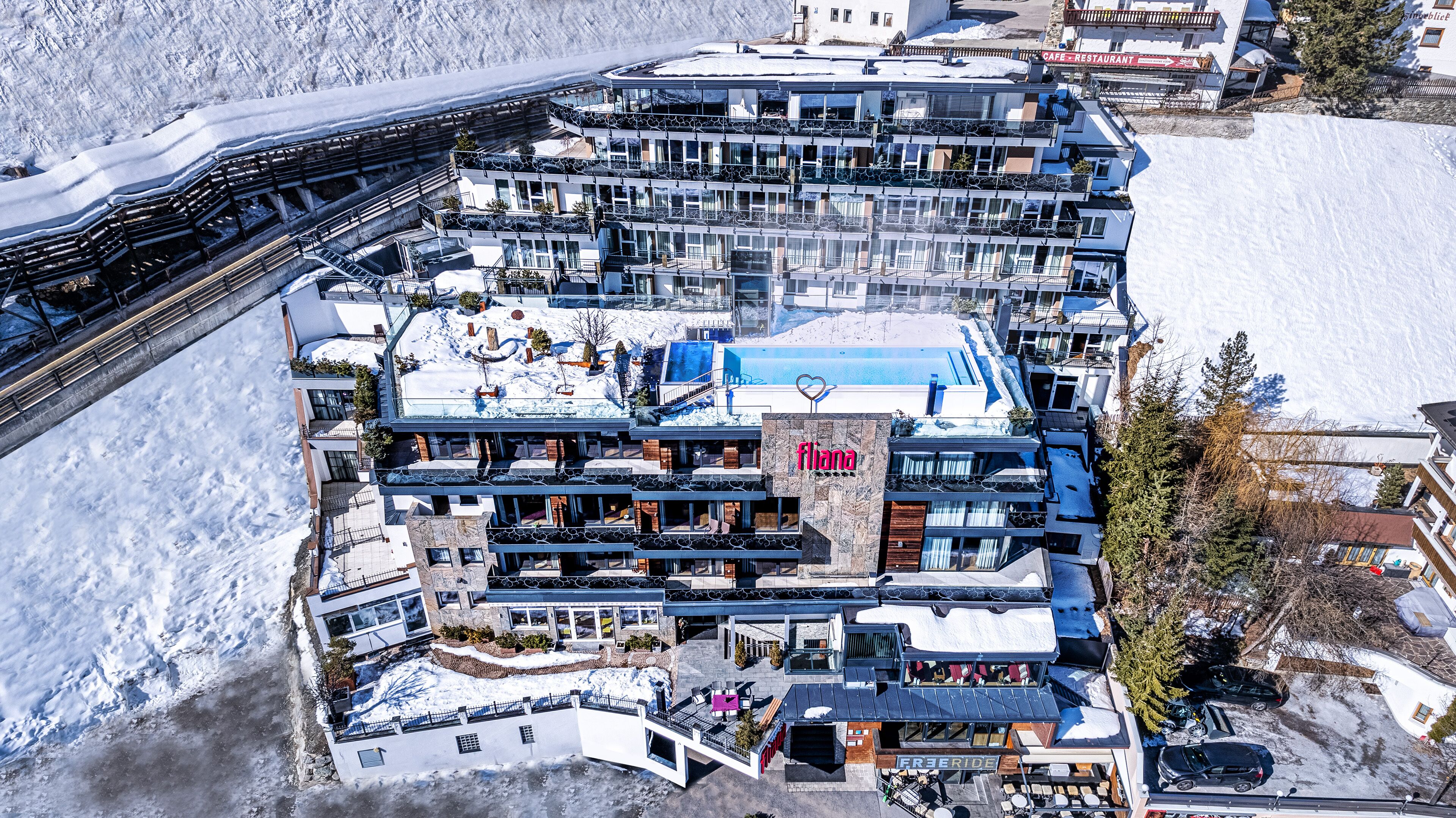 A modern multi-story hotel with balconies, a pool, and a ski lift nearby.