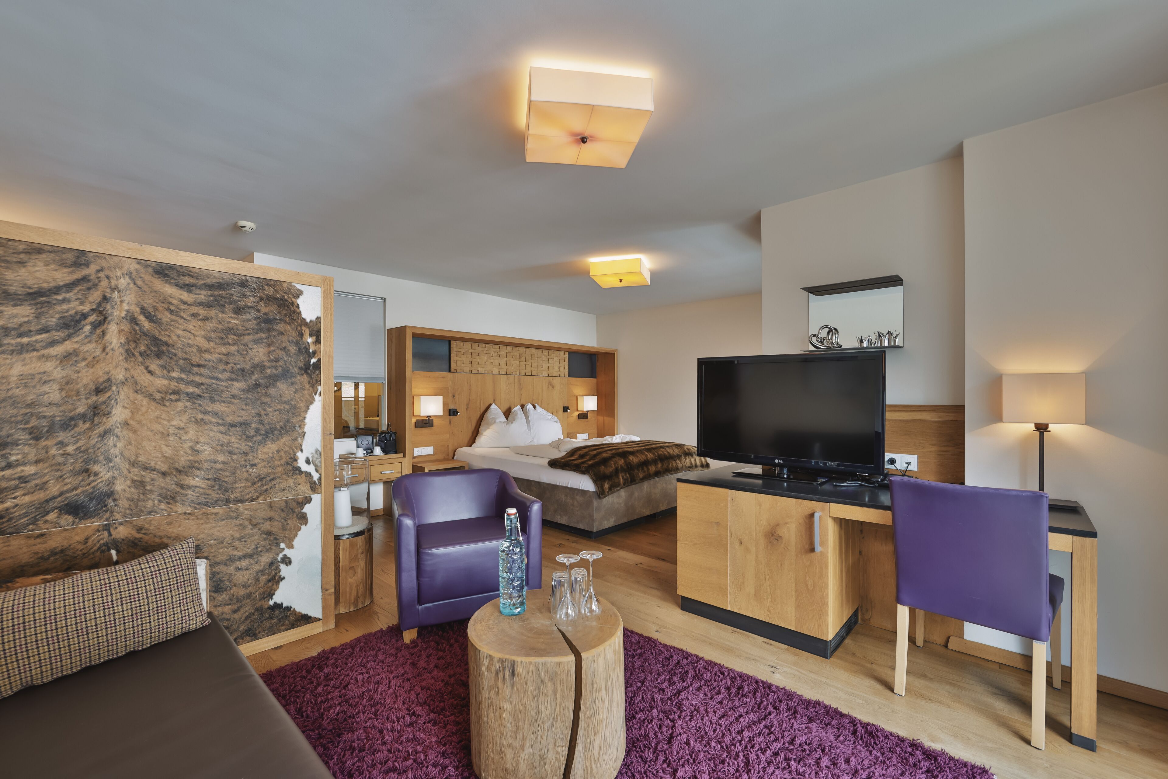 A modern hotel room with a bed, a TV, a desk, and a purple chair.