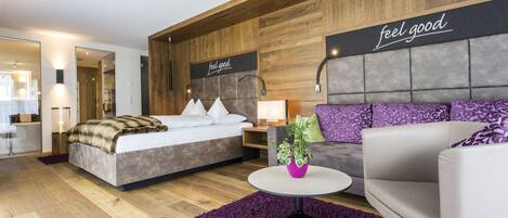 A modern hotel room with a large bed, a sofa, a small table with a plant, and a 'feel good' sign on the wall.