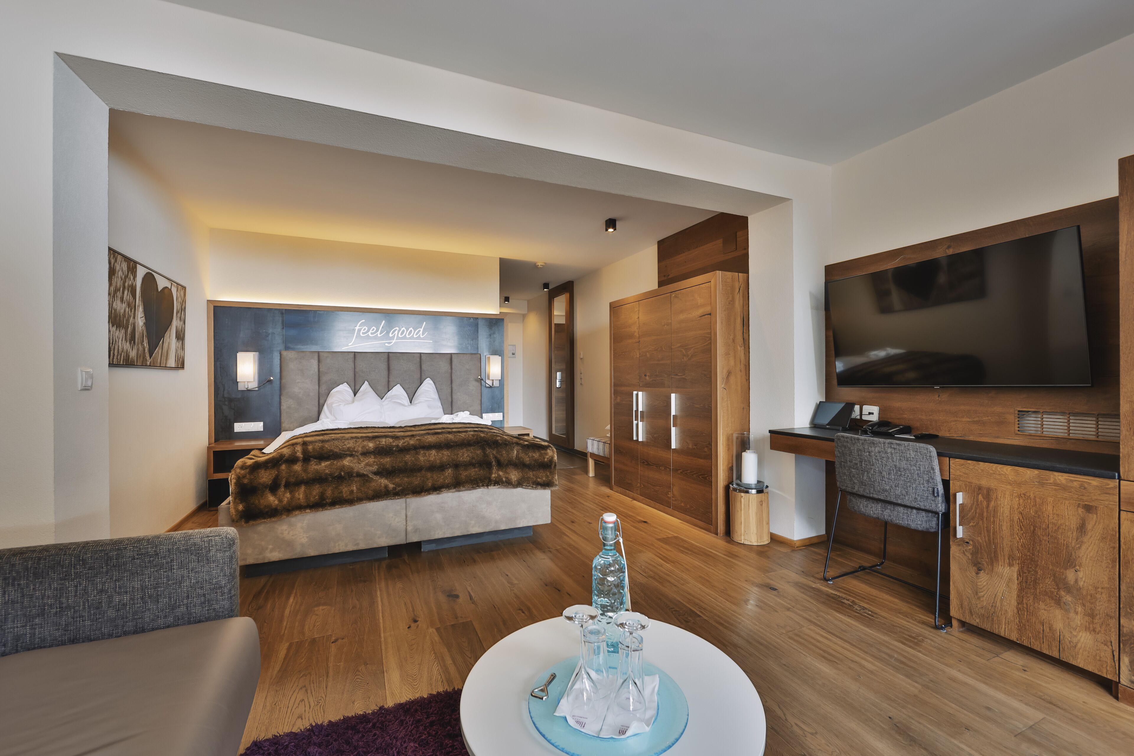 A modern bedroom with a large bed, a desk, and a TV.