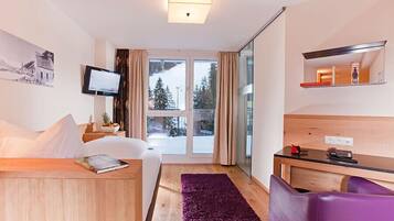 Hotelkamer met een bed, een bureau, een stoel, een televisie en een raam met uitzicht op bomen en een besneeuwd landschap.