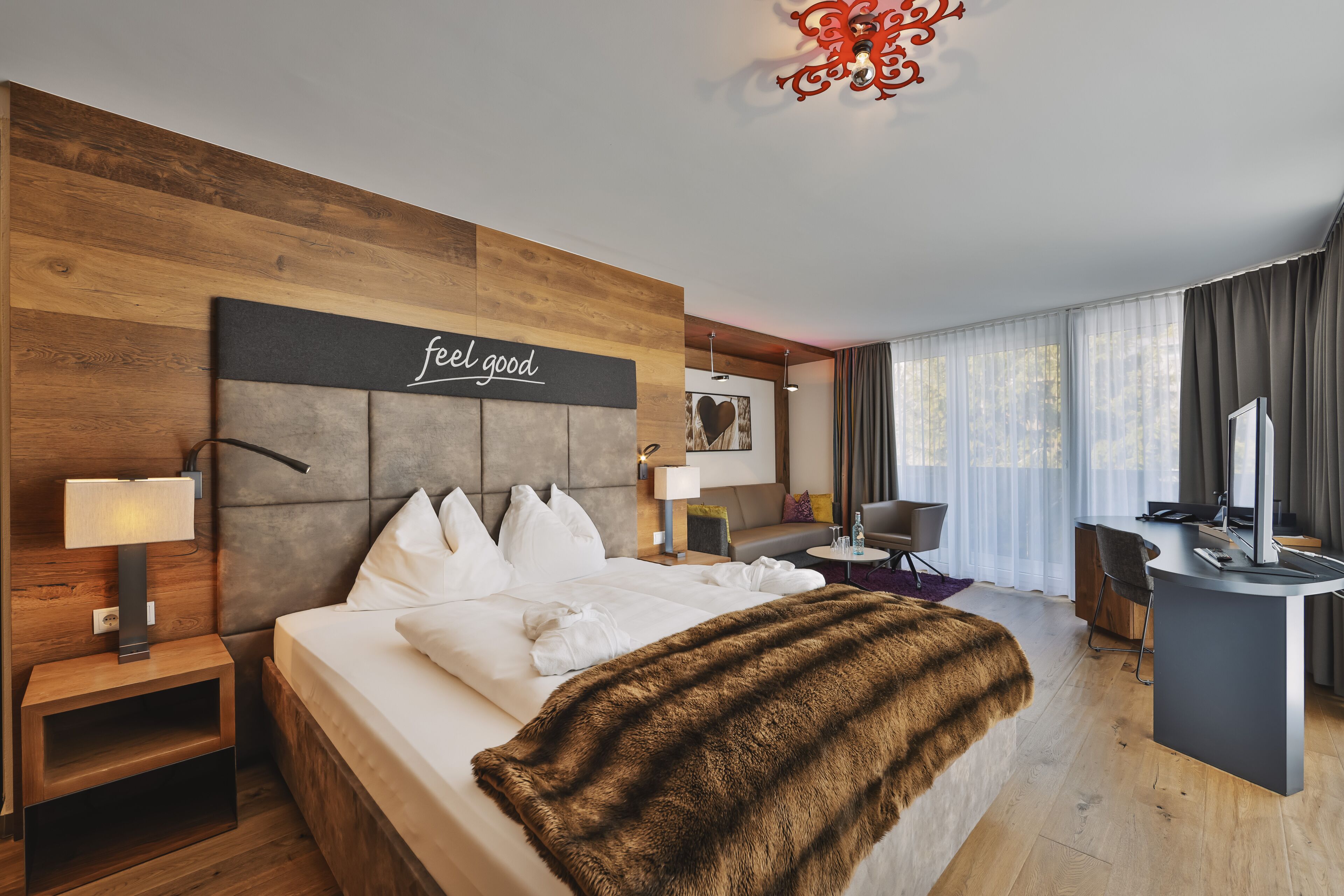 A modern hotel room with a large bed, a desk, a chair, and a television.