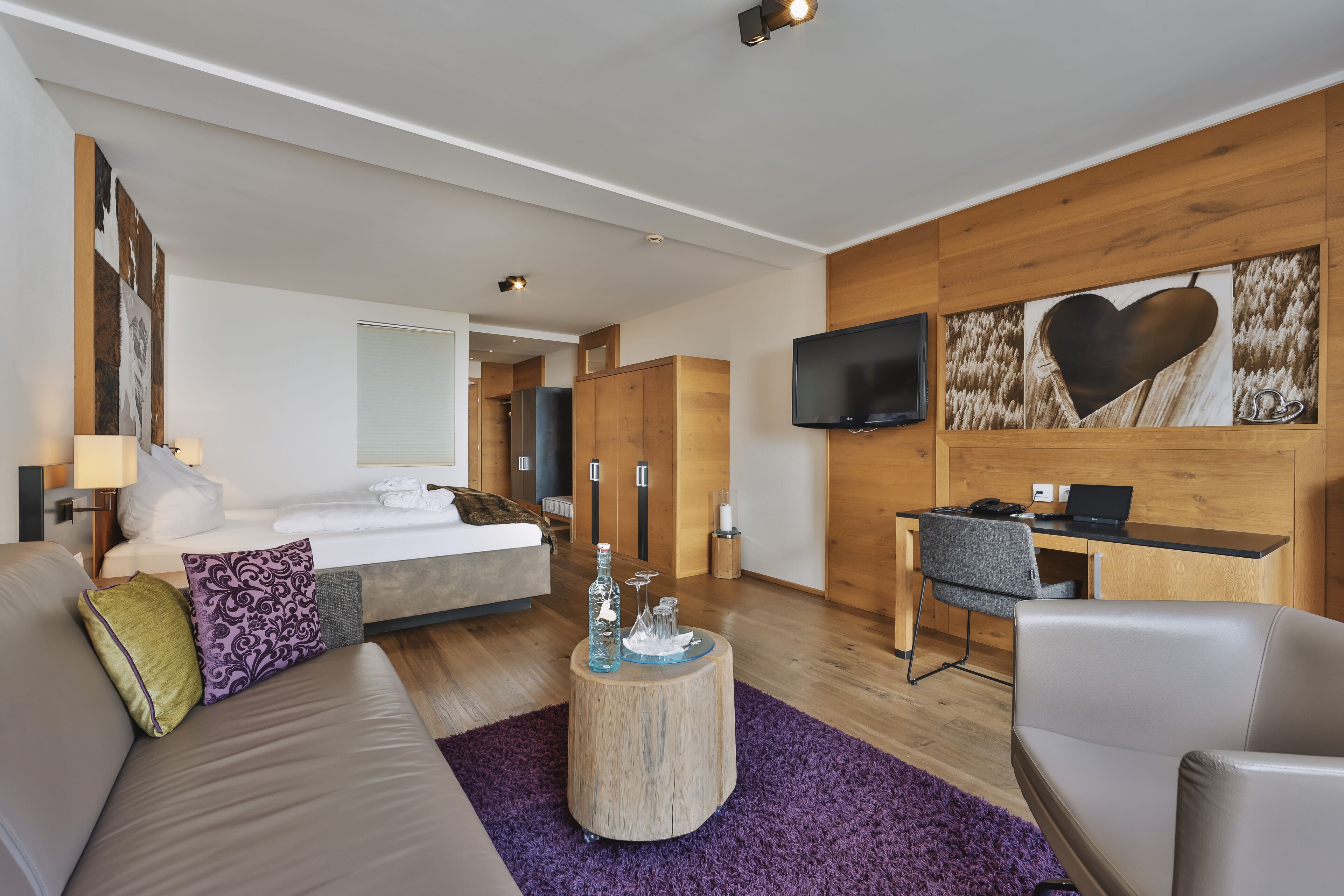 A modern hotel room with a bed, a sofa, a desk, and a TV.