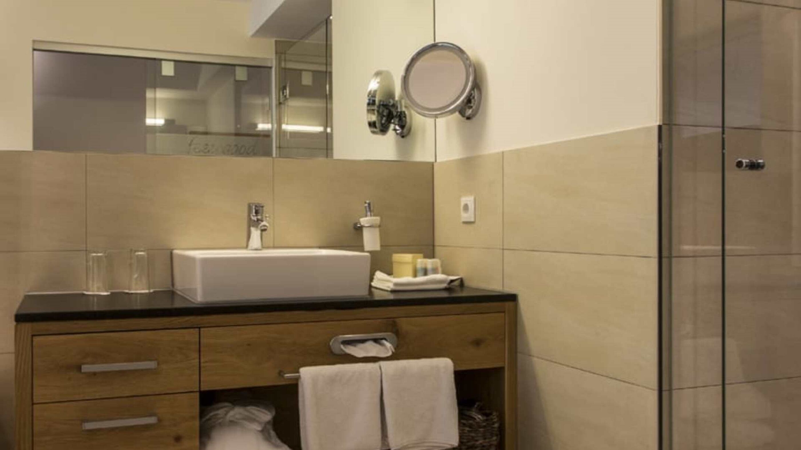 A modern bathroom with a wooden vanity, a white sink, and a glass shower enclosure.