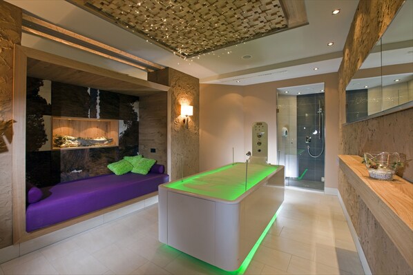 Un moderno espacio de spa con una camilla de masaje, una zona de estar con un sofá púrpura y un mostrador de recepción.