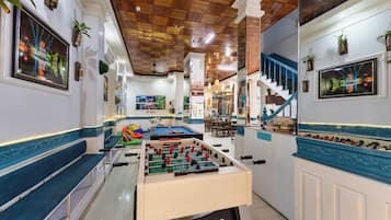 A room with a foosball table, a billiards table, and a pool table. There are multiple seating areas and a staircase.