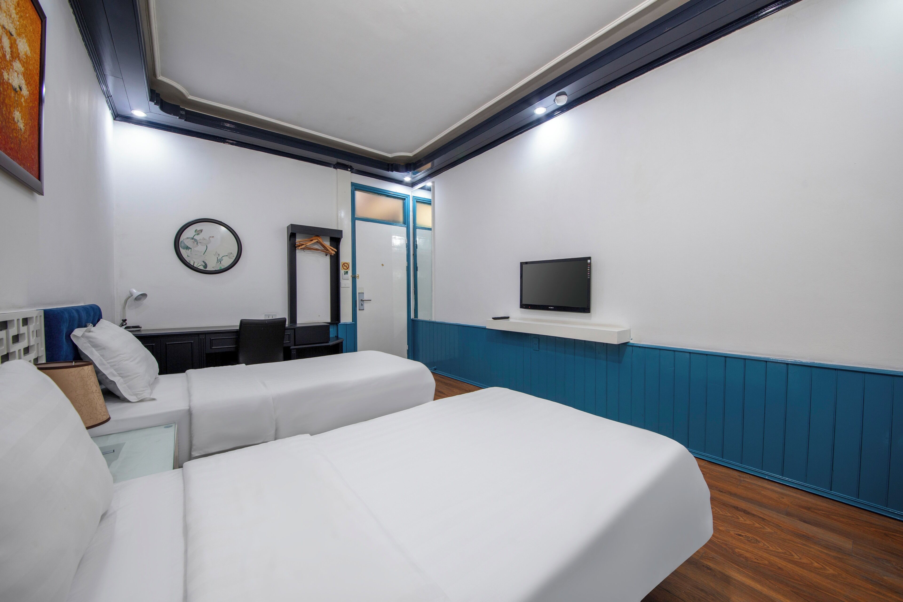 A hotel room with two beds, a desk, a chair, a TV, and a mirror.