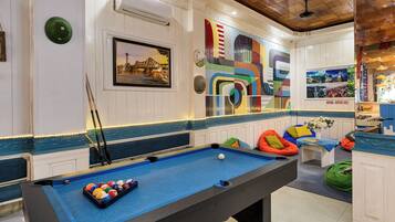 A pool table with balls, a framed picture, and colorful wall art in a room with white walls and blue trim.
