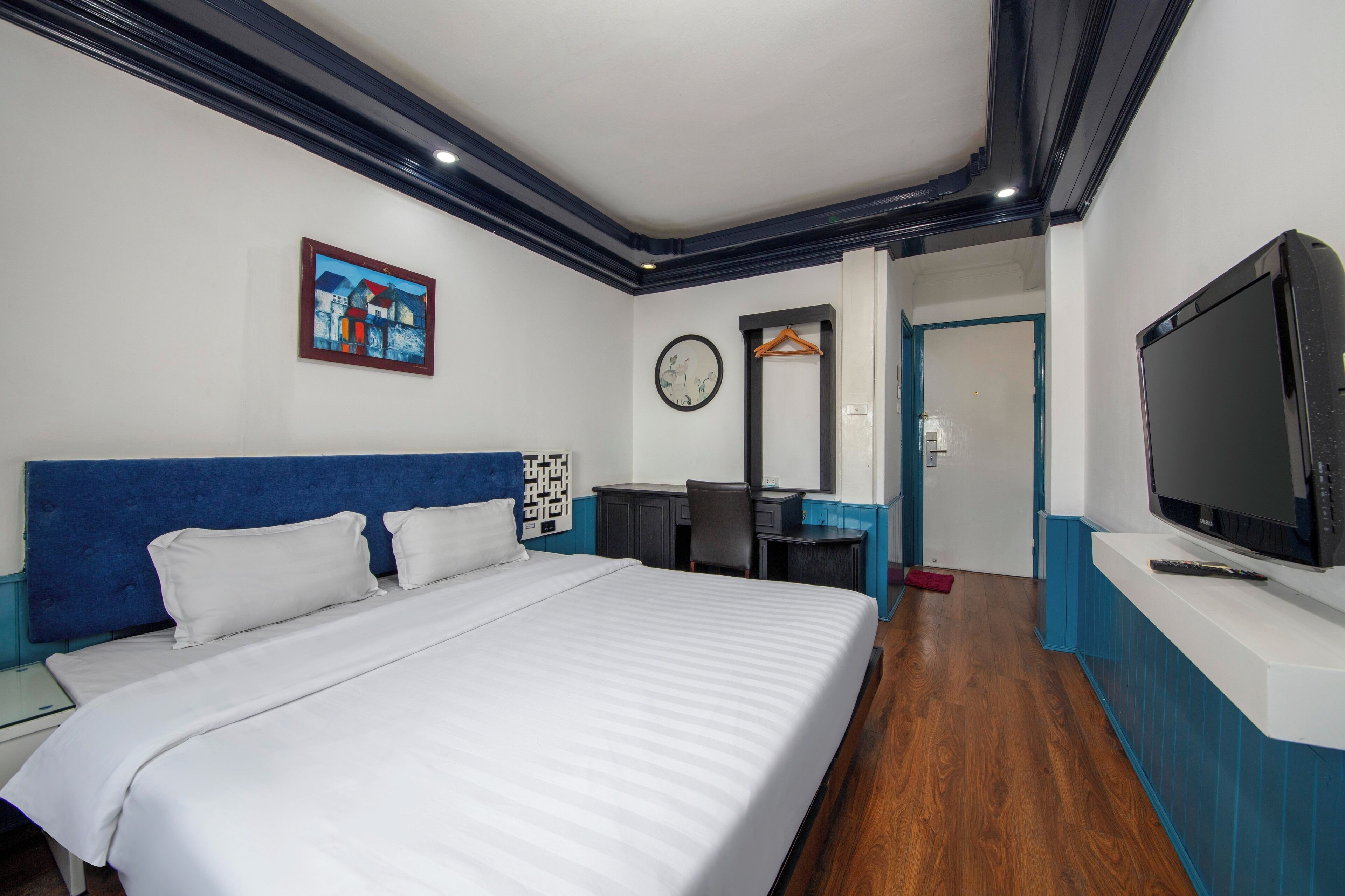 Habitación de hotel con una cama grande, un escritorio con silla, televisión y un reloj de pared.