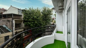 A balcony with a curved railing, a small patch of artificial grass, and a view of neighboring buildings and trees.