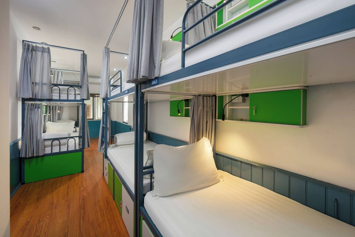 A bunk bed room with a wooden floor, a green and blue color scheme, and a small window.