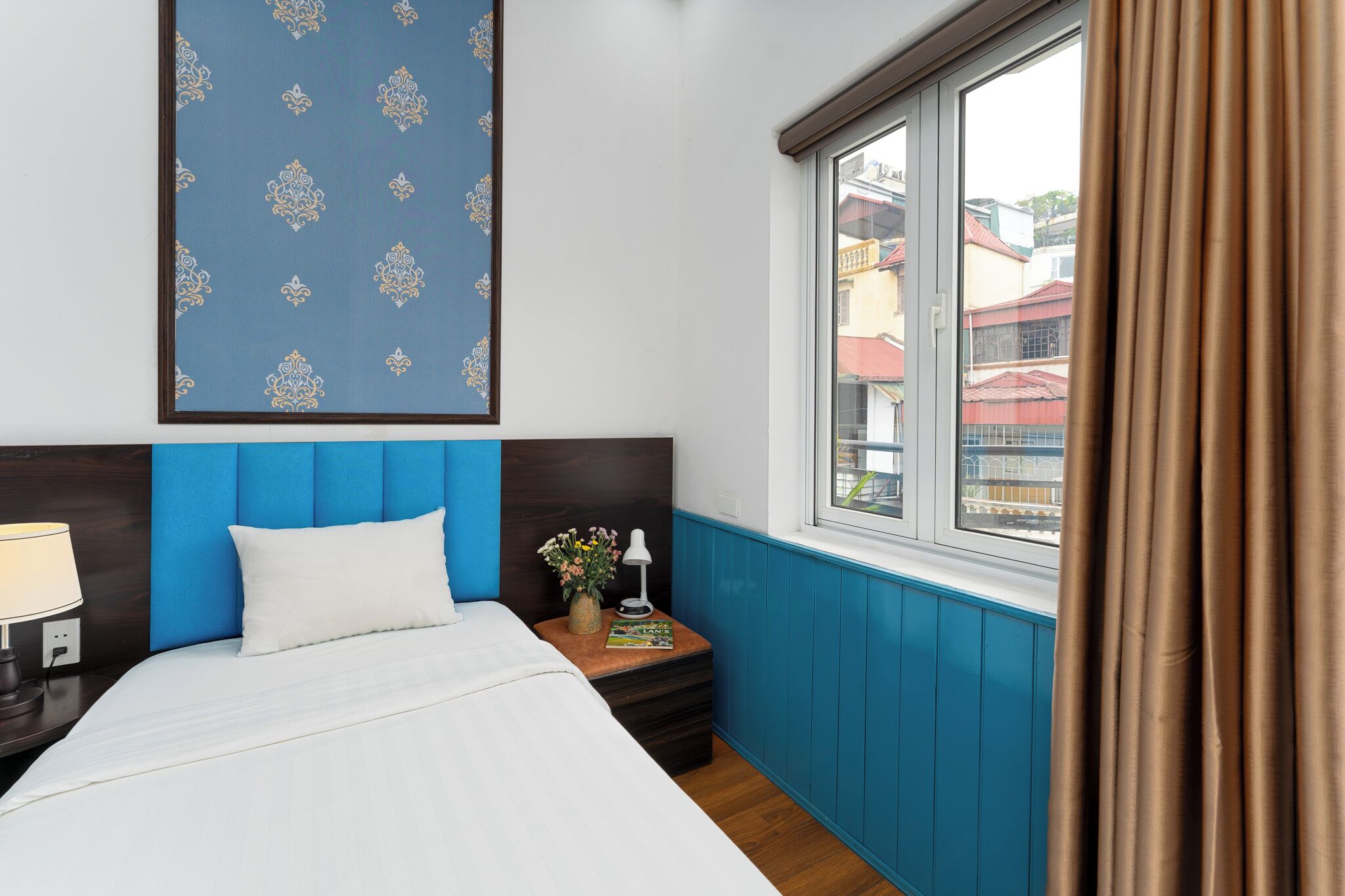 A hotel room with a bed, a nightstand, a window with curtains, and a wall with a patterned wallpaper.