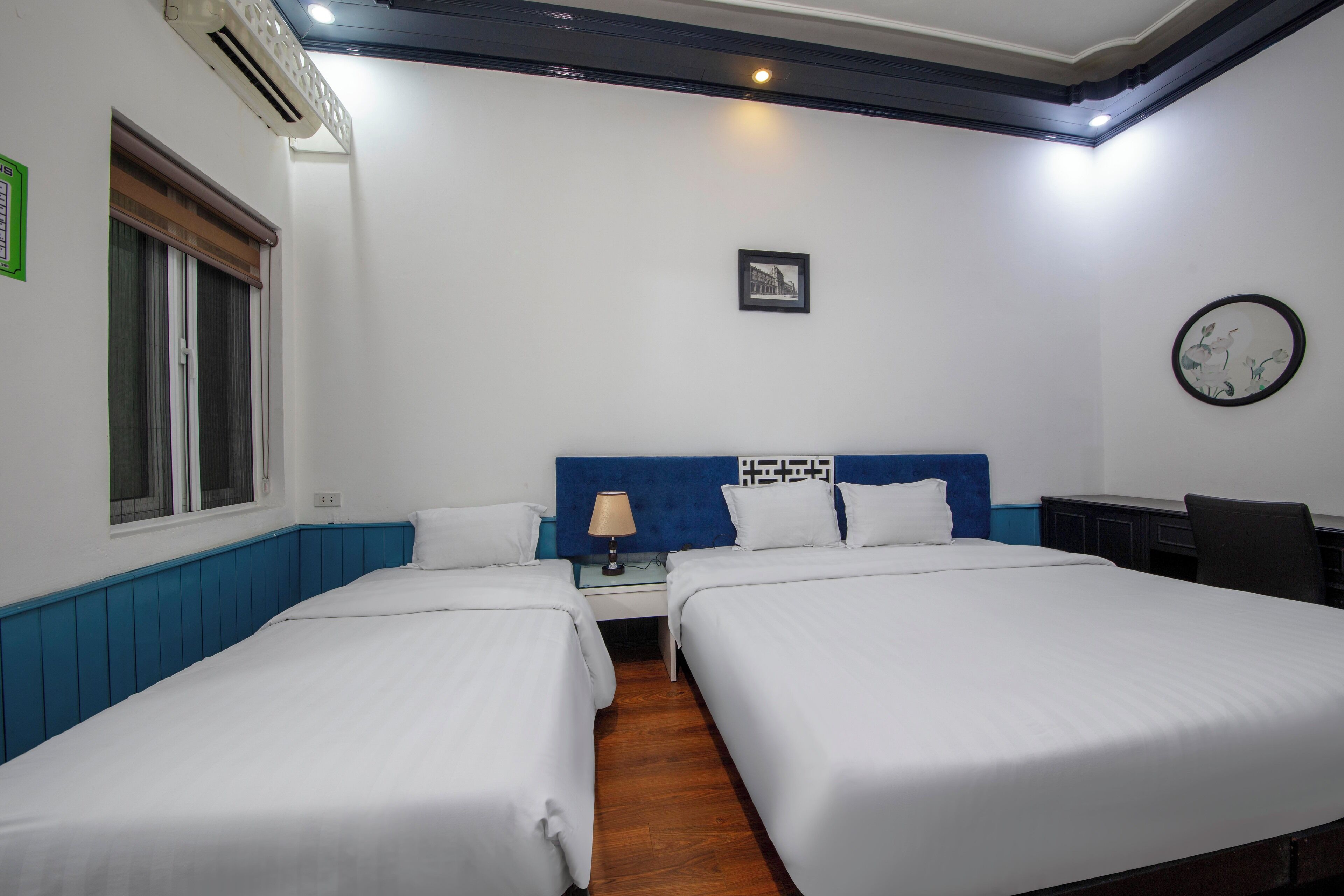 A hotel room with two beds, a desk, a chair, a wall clock, and a picture on the wall.