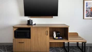 A compact hotel room with a wooden desk, a flat-screen TV, a microwave, and a coffee maker.