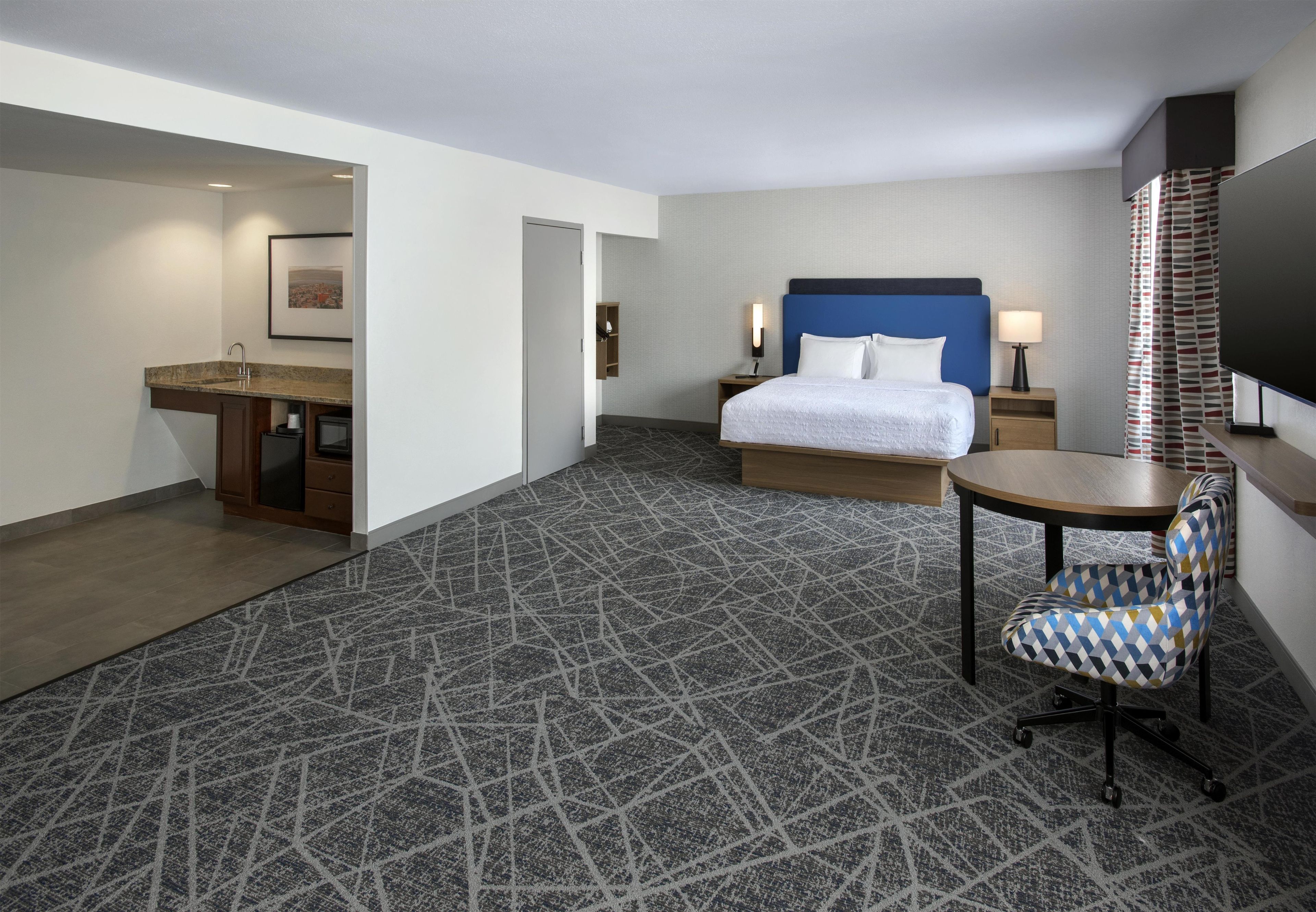 A hotel room with a bed, a desk, a chair, a TV, and a bathroom.