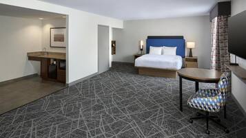 A hotel room with a bed, a desk, a chair, a TV, and a bathroom.