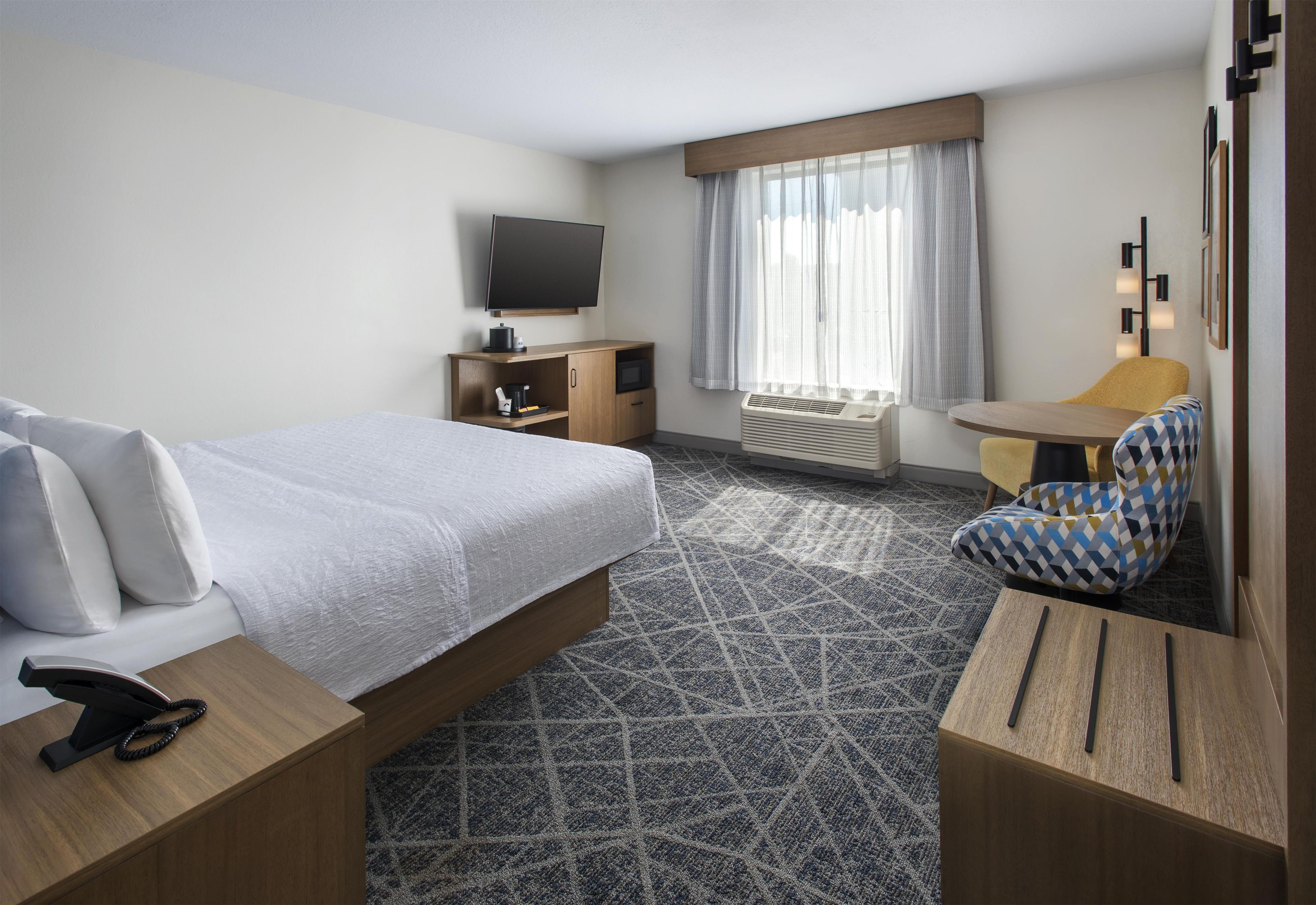A hotel room with a bed, a desk, a chair, a television, and a window with curtains.