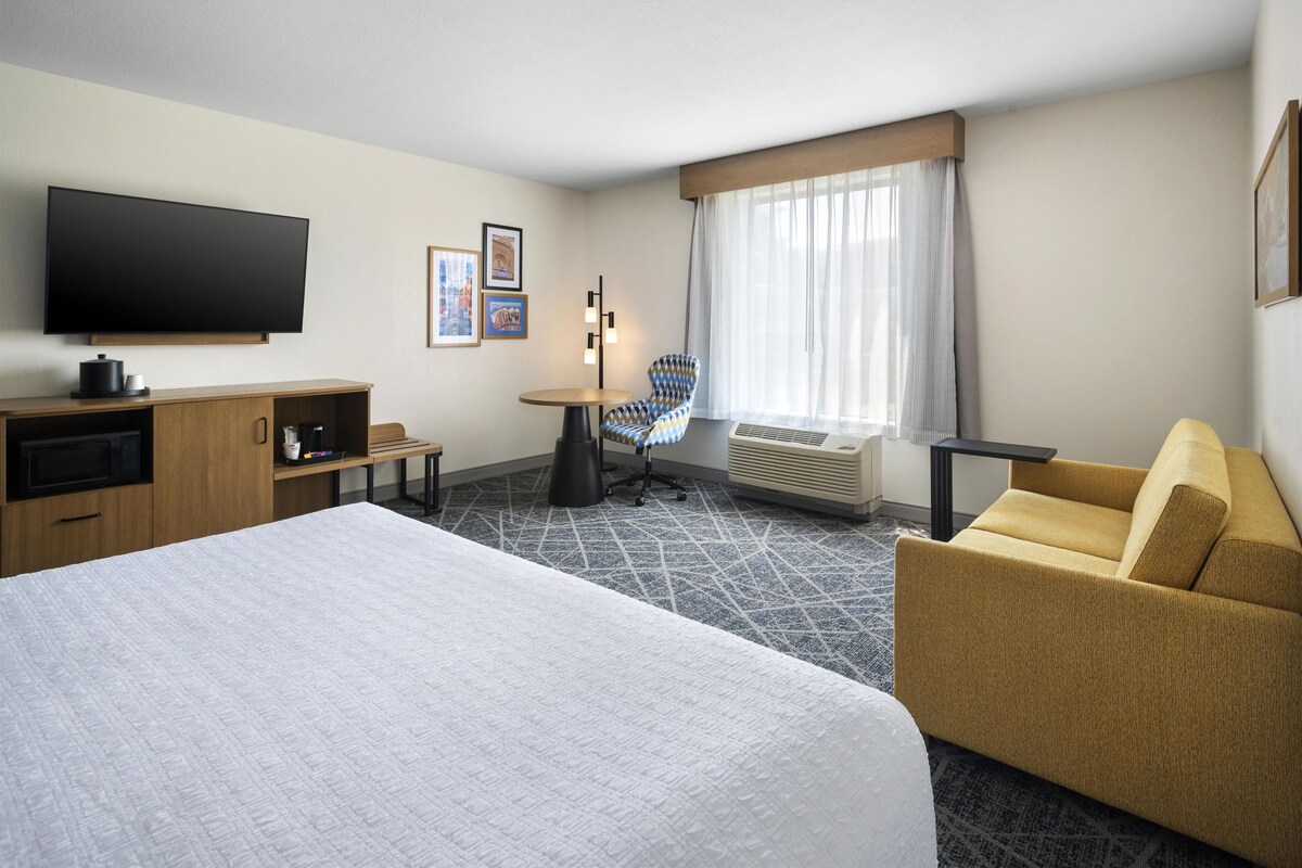 A hotel room with a large bed, a desk, a chair, a television, and a window with curtains.
