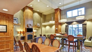 A spacious hotel dining area with wooden furniture, a large window, and a fireplace. - Hampton Inn and Suites New Hartford/Utica (New Hartford)